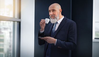 Portrait corporate d'un homme d'affaires senior très élégant portant un costume et la barbe bien taillée dans un bureau et qui boit un café
