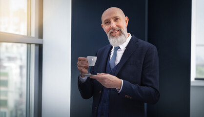 Portrait corporate d'un homme d'affaires souriant qui boit un café debout dans un bureau près d'une fenêtre