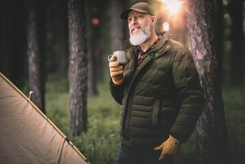 Homme aventurier quinquagénaire qui fait du camping et une randonnée dans la nature avec une tente