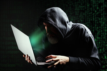 Pirate informatique masqué en train de pirater un ordinateur portable et qui demande une rançon devant un écran vert