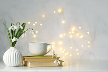 Bouquet of Snowdrop flowers , tea cup and books on table, abstract light background. symbol of...