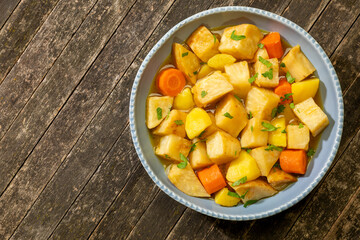 Turkish-style braised celeriac (Zeytinyağlı kereviz) in bowl on rustic wooden table. Copy space.