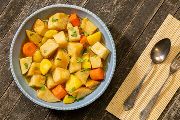 Turkish-style braised celeriac (Zeytinyağlı kereviz) in bowl on rustic wooden table. Knife and fork on a bamboo mat next to it. 