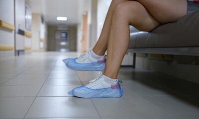 Woman in shoe covers sitting in hospital corridor closeup. Sanitary norms of behavior in medical...