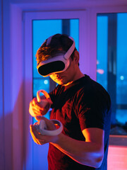 A young man in a virtual reality headset and gamepads with controllers, playing a shooting game. Modern technology, play VR video games.