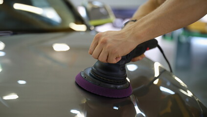 Male hands polishing hood of car with special machine closeup. Car repair and maintenance concept