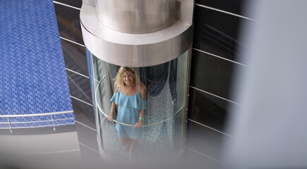 Young woman riding in glass transparent elevator in hotel. Modern technologies concept