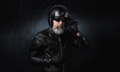 Portrait d'un motard homme avec un casque et une veste en cuir et des lunettes de protection et une barbe grise vintage