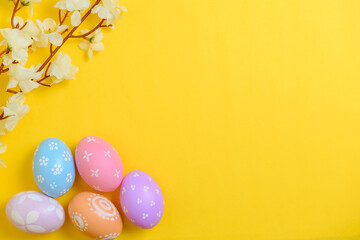 Happy Easter holiday greeting card design concept. Colorful Easter Eggs and spring flowers on yellow background. Flat lay, top view, copy space.