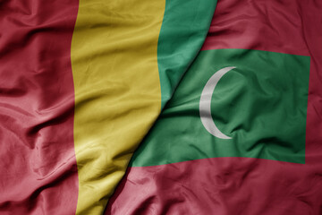 big waving national colorful flag of maldives and national flag of guinea .
