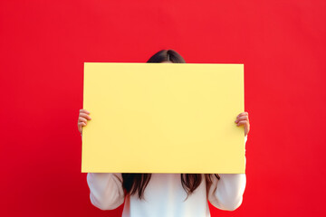 Obraz premium Portrait of a woman holding a blank yellow sign on a red background