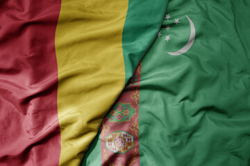 big waving national colorful flag of turkmenistan and national flag of guinea .