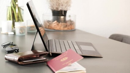 Man typing on laptop with German passport and wallet in frame