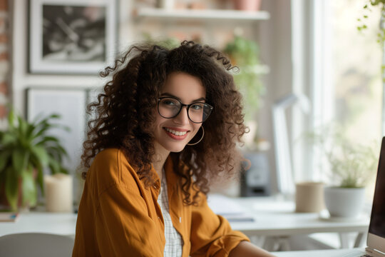 Bright Workspace and Curly Smiles. Curly-haired woman with glasses, cheerful in a sunny, plant-filled home office.