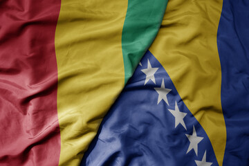 big waving national colorful flag of bosnia and herzegovina and national flag of guinea .
