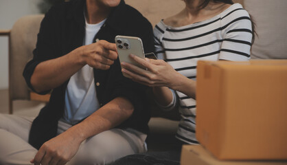 Two Asian blogger showing clothes in front of the camera to recording vlog video live streaming at her shop. Online Shopping Cart notion. on sofa at home