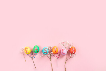 Easter flat lay composition with colorful painted natural eggs with text 'Easter' on them and flowers
