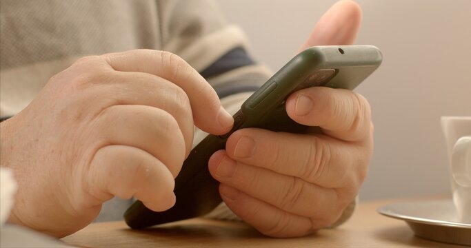 Senior man using contactless payment at a cafe through a mobile application. Modern method of payment involves utilizing mobile app on a smartphone to complete transactions. Seniors hands close-up. - Powered by Adobe