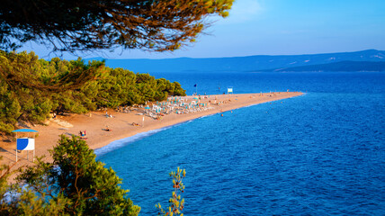 “Zlatni rat“ panorama – popular and famous beach in Bol on Brac island in Croatia. Sandy spit of land or tongue reaching into adriatic sea (Mediterranean Sea) at sunset with warm light in summer.