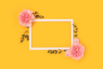 Frame made of pink carnation flowers and green eucalyptus branches on a yellow background. Floral layout.