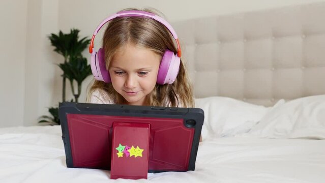 Emotion excited surprise child in headphones playing digital tablet computer home. Application for children development. Toddler watch interesting learning video, movie, online class, listen to music