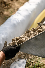 Drainage works for drainage of ground water. A man pours rubble crushed stone from a wheelbarrow into a trench close up.