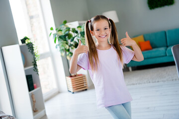 Portrait of sweet friendly girl toothy smile hands fingers demonstrate thumb up approval bright apartment indoors