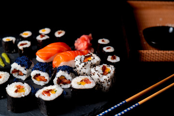 Japanese food on black plate and black background. Sushi board with soy sauce and chopsticks. Dish on black background