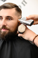 Barber shaves the temple with cordless trimmer during a short haircut on the sides of the head.