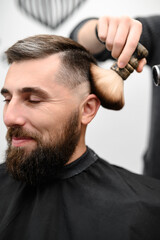 Fototapeta premium Barber sweeps hair with a brush while cutting a client hair in a salon.
