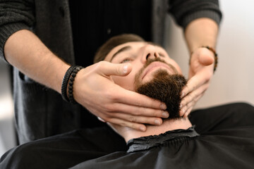 A barber massages and rubs a male client beard after applying moisturizing oil