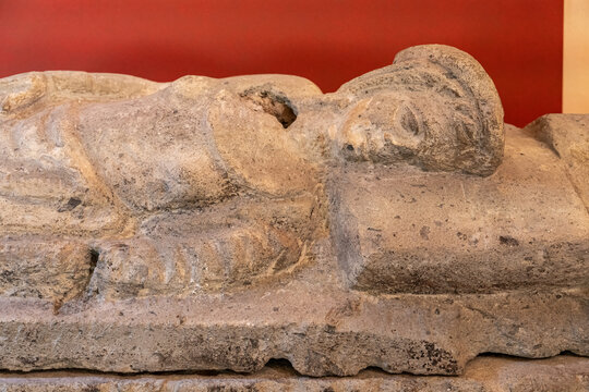 Close-up on ancient statue carved in stone showing a woman laying on a tomb