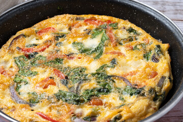 Italian Frittata made with spinach, tomatoes, onion and peppers on white wooden table