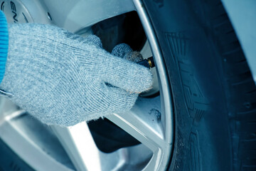 Hand holds the pressure gauge and fills the car tires with air. Car maintenance. - obrazy, fototapety, plakaty