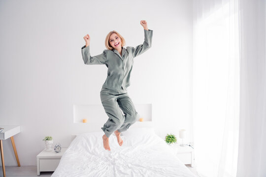 Photo portrait of pretty blonde young girl jump bed have fun celebrate wear trendy gray nightwear bright bedroom interior design