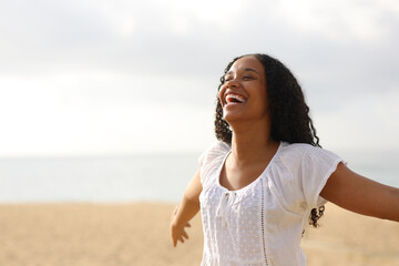 Joyful black woman outstretching arms on the beach - obrazy, fototapety, plakaty