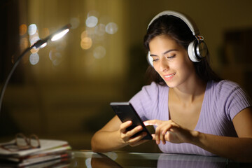Happy woman in the night using phone weraring headphone - 724646030