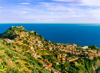 scenic view from highland to a mountain town with beautiful buildings, castles, hills and slopes and panoramic sea gulf with cloudy sky on background