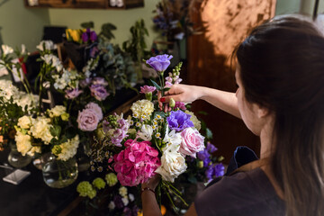 Young woman working in her flower shop making bouquet with various types of flowers.