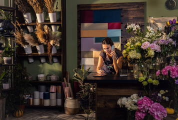Young woman working in her flower shop talking on the phone and receiving an order for a bouquet of flowers.