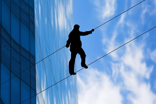 Silhouette of person tightrope walking against blue sky on building