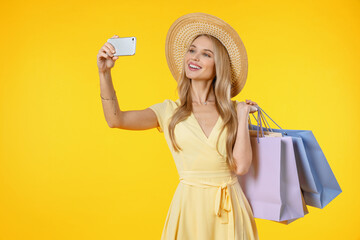 Amazing young woman posing isolated over yellow background holding shopping bags take selfie by...