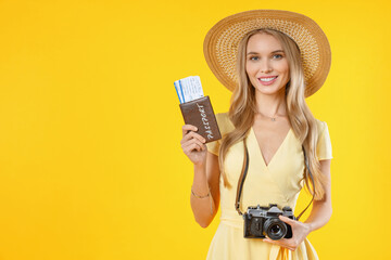 Cute girl with retro camera on neck holding airline ticket isolated on yellow background. Trip...