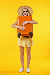 Vertical shot of young woman over isolated yellow background in vacation with travel suitcase. Caucasian female traveler explorer ready to go on voyage trip holiday