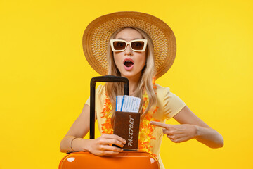 Young surprised woman over isolated yellow background in vacation with suitcase and passport. Tourist going on a holiday voyage trip in hot summer resort abroad