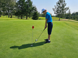 Fototapeta premium Boy plays golf on the putting green and hits ball into hole
