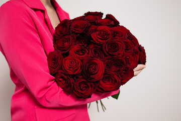 Woman in pink jacket with luxurious mono bouquet of red roses on grey background. Surprise gift for...
