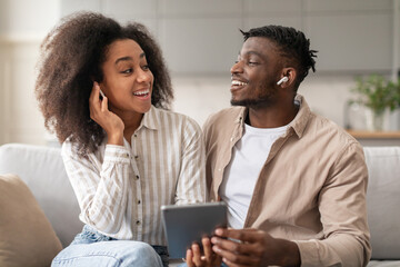 black couple listening music on digital tablet wearing earbuds indoor
