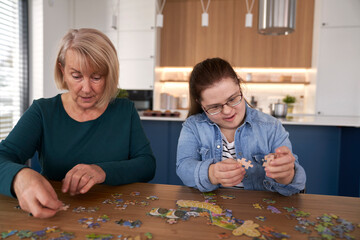 Focus down syndrome woman and her mother assembling puzzles at home