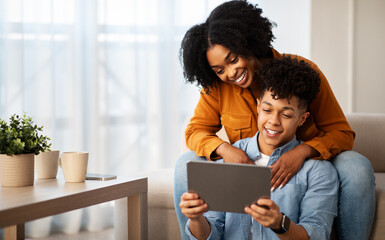 Happy young african american man and lady, hugs, use tablet, watch video on device